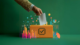 A conceptual image of a ballot box in orange with a checkmark icon on the front. A hand is placing a ballot into the box, while data visualizations like charts and graphs emerge around it against a green background. The image conveys themes of data transparency and informed decision-making