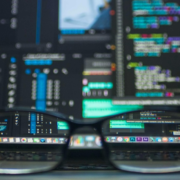 glasses in foreground with data processing on screens behind it