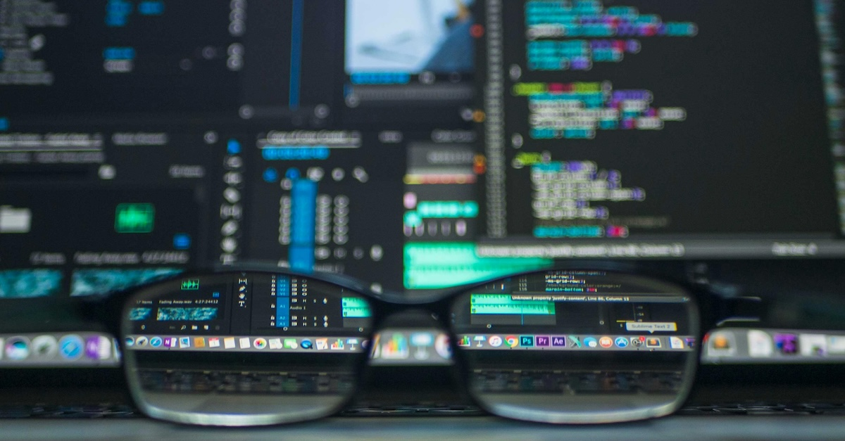 glasses in foreground with data processing on screens behind it